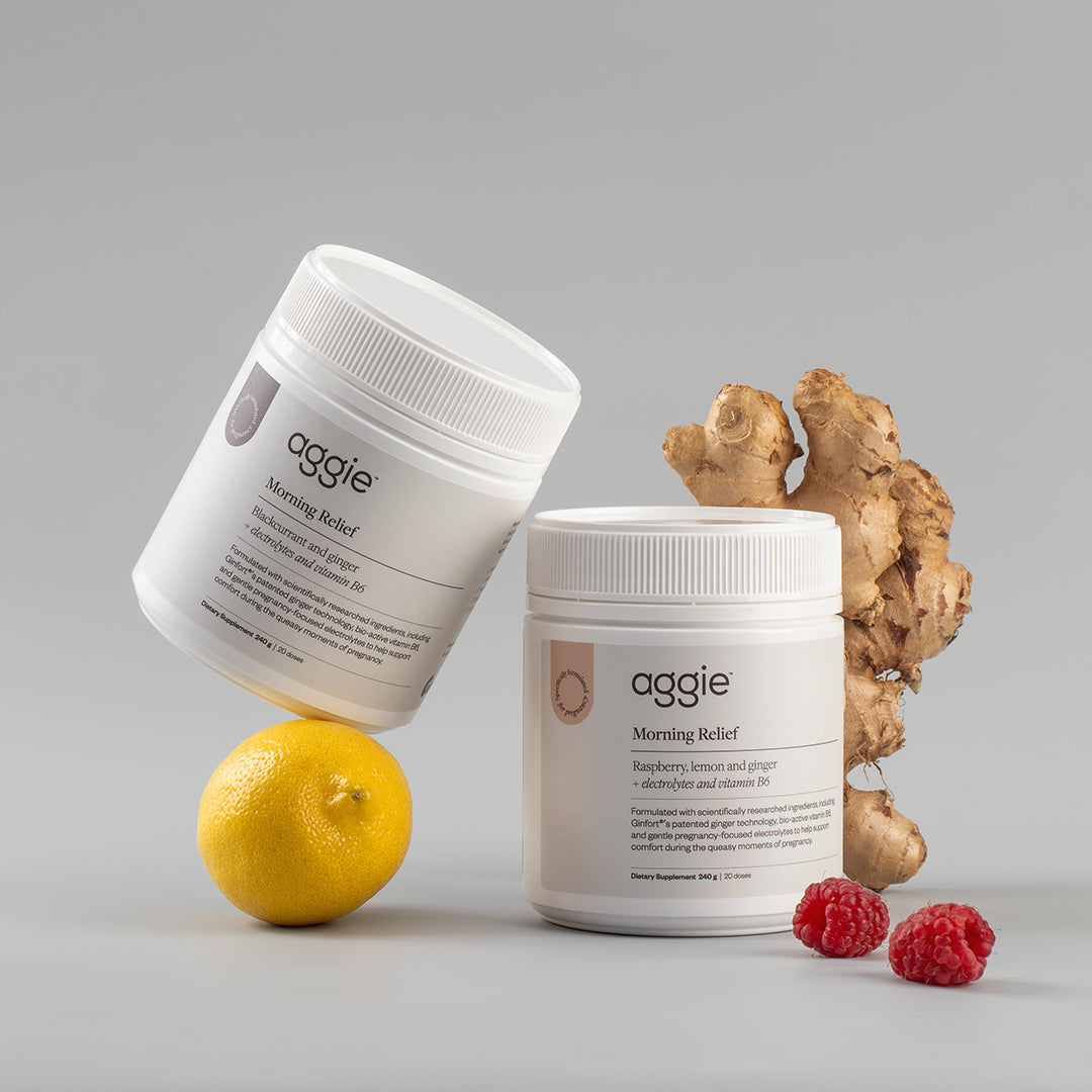 Two containers of 'aggie' brand product with a lemon, ginger root, and raspberries on a gray background. Morning Relief support pregnancy sickness, morning sickness, hyperemesis gravidarum nausea and vomiting during pregnancy.
